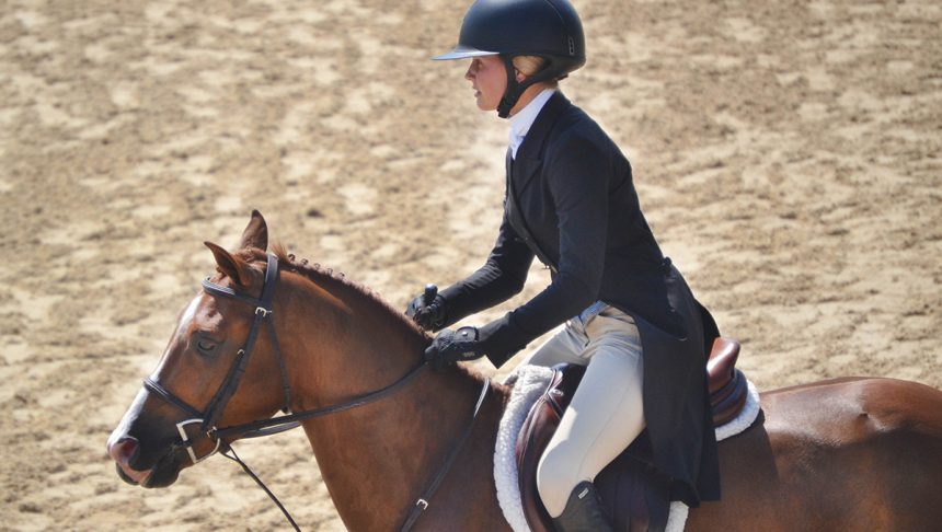 A girl riding a horse and wearing proper attire, including a riding helmet